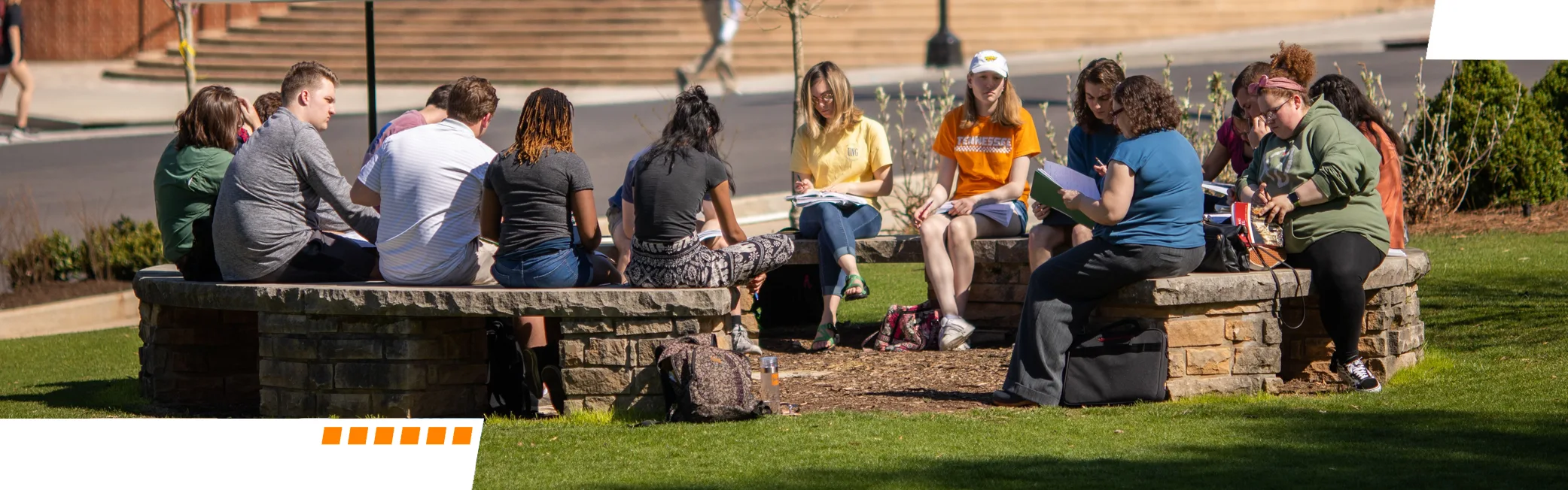 Photograph of a group of students having a discussion on a set of round benches in an outdoor setting. 